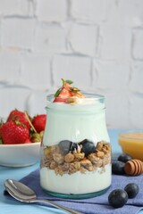 Tasty yogurt with granola, berries, honey and spoon on light blue table, closeup