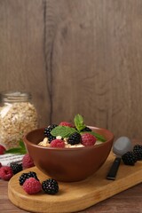 Tasty yogurt with granola and berries in bowl on wooden table, closeup. Space for text