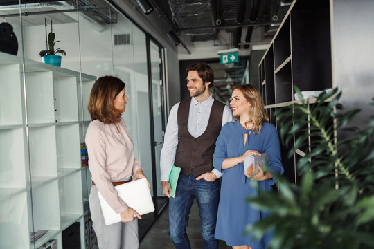 Group of coworkers standing in office corridor and talking. - Powered by Adobe