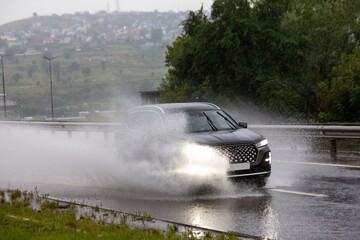 A car drives on a road flooded by rain. Heavy rainfall, climate change.