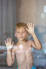 Little child, boy behind the window in a bathroom, looking outside