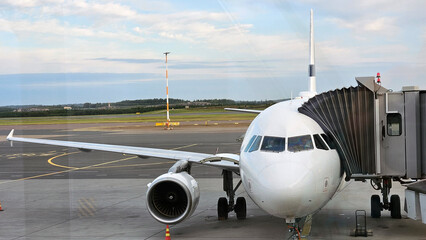 Airplane with passenger jet bridge attached. View from the airport window