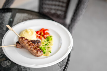 Grilled sausages on skewers with mashed potatoes, cherry tomatoes, and herbs served on a white...