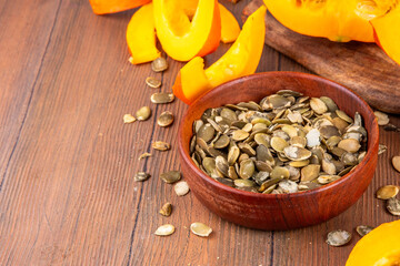 Homemade organic dried pumpkin seeds with fresh raw pumpkin squash slices, on wooden table...