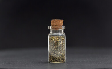 Dry green tea in glass container in front of black background.