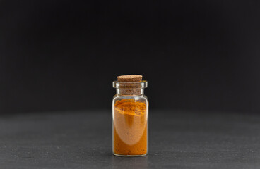 Closeup of gold colored dry turmeric powder in glass vial container in front of black background. 