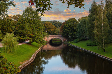 Small bridge on the canal among trees in the urban park in Riga.