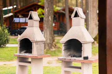 Two outdoor stone barbecue grills with chimney features are positioned on a grassy area, surrounded...