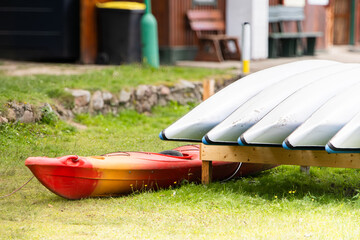 Bright red kayak resting on green grass beside stacked white kayaks on wooden rack, showcasing...