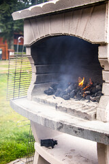 Outdoor barbecue grill with glowing coals and smoke rising, surrounded by green grass, creating a...