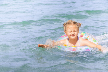 Young girl with playful expression is swimming in clear blue water, enjoying summer fun while...