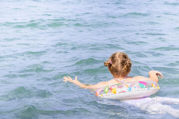 Young girl with braided hair is floating on a colorful inflatable ring in a serene blue ocean,...