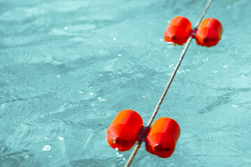 Bright orange buoys float on the surface of a clear blue swimming pool, creating a vibrant contrast...