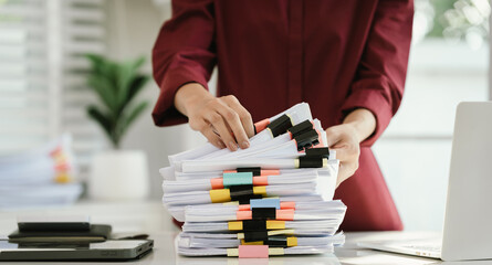A woman in a red shirt is handling a large number of documents and files, symbolizing office work,...