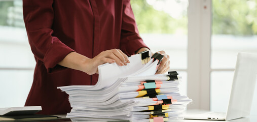 A woman in a red shirt is handling a large number of documents and files, symbolizing office work,...