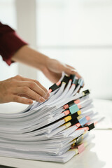 A woman in a red shirt is handling a large number of documents and files, symbolizing office work,...