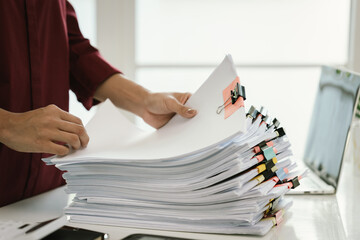 A woman in a red shirt is handling a large number of documents and files, symbolizing office work,...