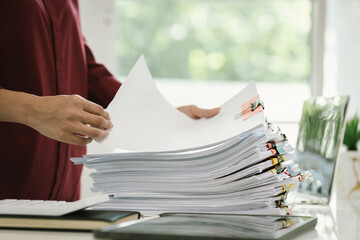 A woman in a red shirt is handling a large number of documents and files, symbolizing office work,...