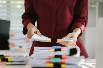 A cluttered office desk filled with paperwork, documents, files, and reports, symbolizing heavy...