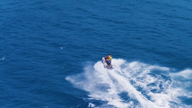 Two individuals ride a jet ski across vibrant blue waters near Voulisma Beach, Crete. The jet ski leaves a white foam trail under clear, sunny skies.