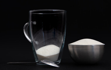 Collagen powder in metal container bowl with spoon next to a glass of collagen powder, in front of...