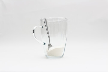 Closeup of spilled collagen powder, that is in a glass of collagen with spoon in it and white...