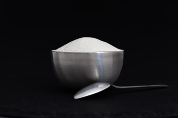 Dry collagen powder in spoon and metal container in front of black background. Version 3.