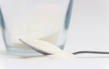 Closeup of spilled collagen powder, that is spilled out from spoon in front a glass of collagen and...