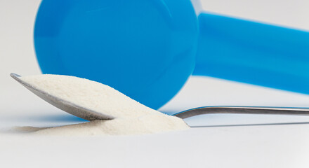 Spilled, dry collagen powder in spoon in front of blue plastic measuring spoon with white...
