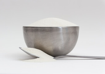 Dry, spilled collagen powder in spoon and metal container in front of white background. Version 3.
