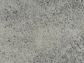grey hard surface of concrete or cement or hardened mortar with round pits or bubbles, background texture of concreted or asphalted pavement with a lumpy structure
