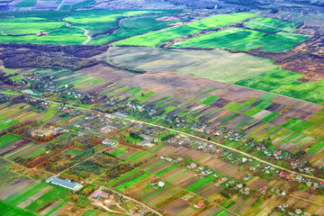 Aerial view of rural landscape with patchwork agricultural fields and tiny houses along road, farms, plant, lumberyard, school