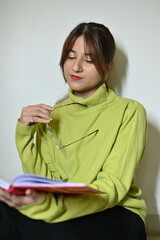 young woman with a book in hands. young woman reading a book. glasses in hands. white wall. time to read. enjoy with a book