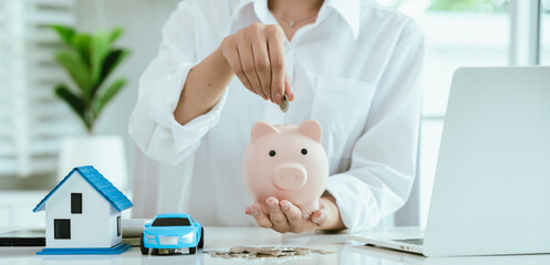 A business concept showing hands holding a house and car models with stacked coins, symbolizing...