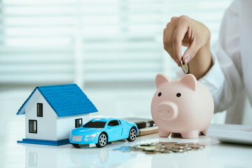 A business concept showing hands holding a house and car models with stacked coins, symbolizing...