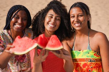 Young multiracial women smiling and holding fresh watermelon on camera at the beach - Summer, vacation and lifestyle concept