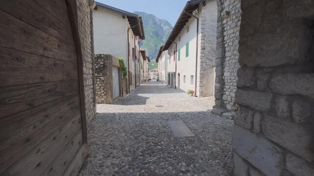 First-person view walking through a medieval stone arch into a narrow cobbled street of Venzone, Italy. Concept of exploration, slow travel and authentic European heritage