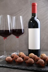 Tasty truffle bonbons and red wine on grey textured table, closeup