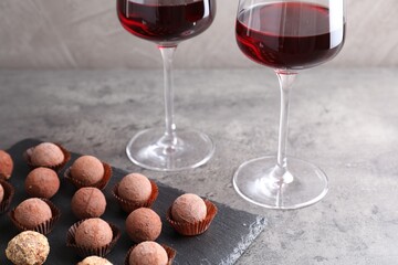 Tasty truffle bonbons and red wine on grey textured table, closeup