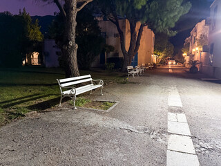 White benches line a quiet alley illuminated by warm lanterns in the evening town. Silence, rest...