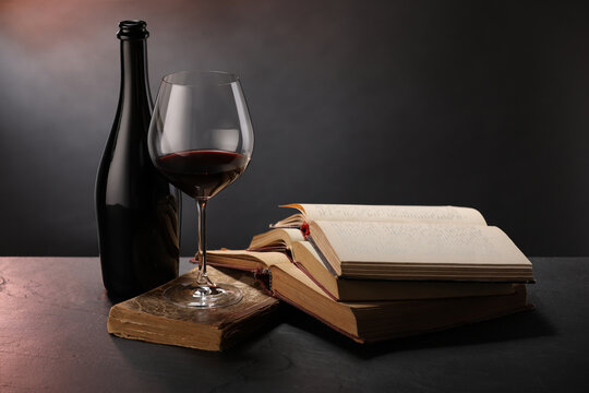Tasty wine and books on dark textured table in color light, closeup