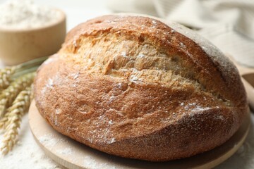 Loaf of fresh bread, flour and spikes on table, closeup