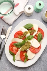 Tasty salad Caprese served with pesto sauce on grey table, flat lay