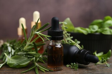 Bottles of aromatic essential oils and herbs on wooden table against brown background, closeup
