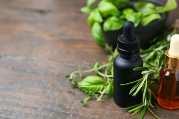 Bottles of aromatic essential oils and herbs on wooden table, closeup. Space for text