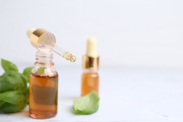 Bottles of aromatic essential oils and herbs on white textured table, closeup. Space for text