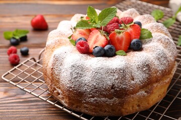 Tasty Bundt cake with powdered sugar and berries on wooden table, closeup