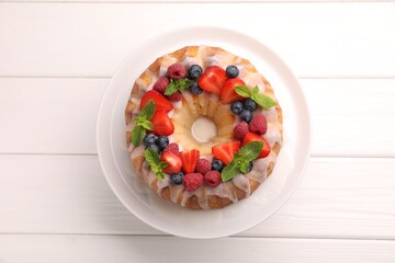 Delicious bundt cake with berries, glaze and mint on white wooden table, top view