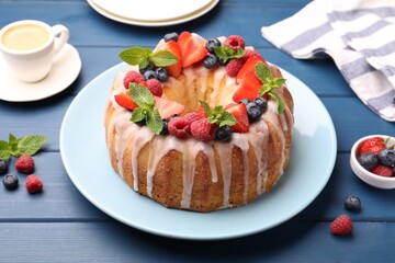 Delicious bundt cake with berries, glaze and mint on blue wooden table, closeup