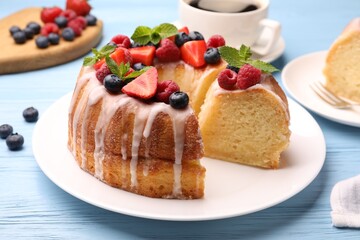 Pieces of delicious bundt cake with berries, glaze and mint on light blue wooden table, closeup